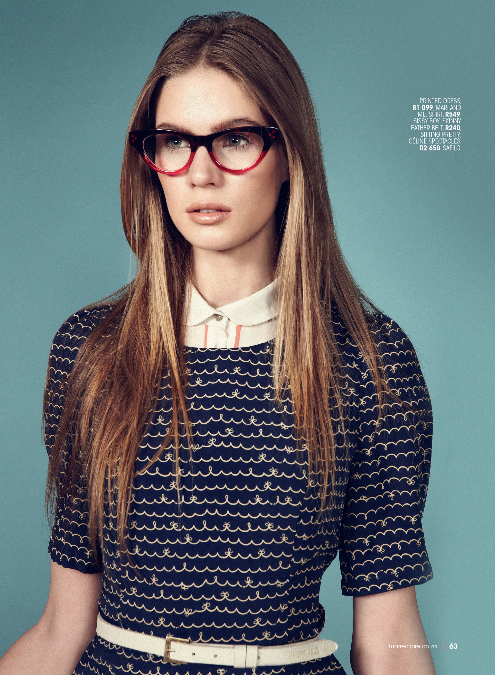 Young woman in a navy printed dress with wave patterns, wearing red-rimmed glasses, accessorized with a white belt, against a teal background. Fashion shoot for Marie Claire.