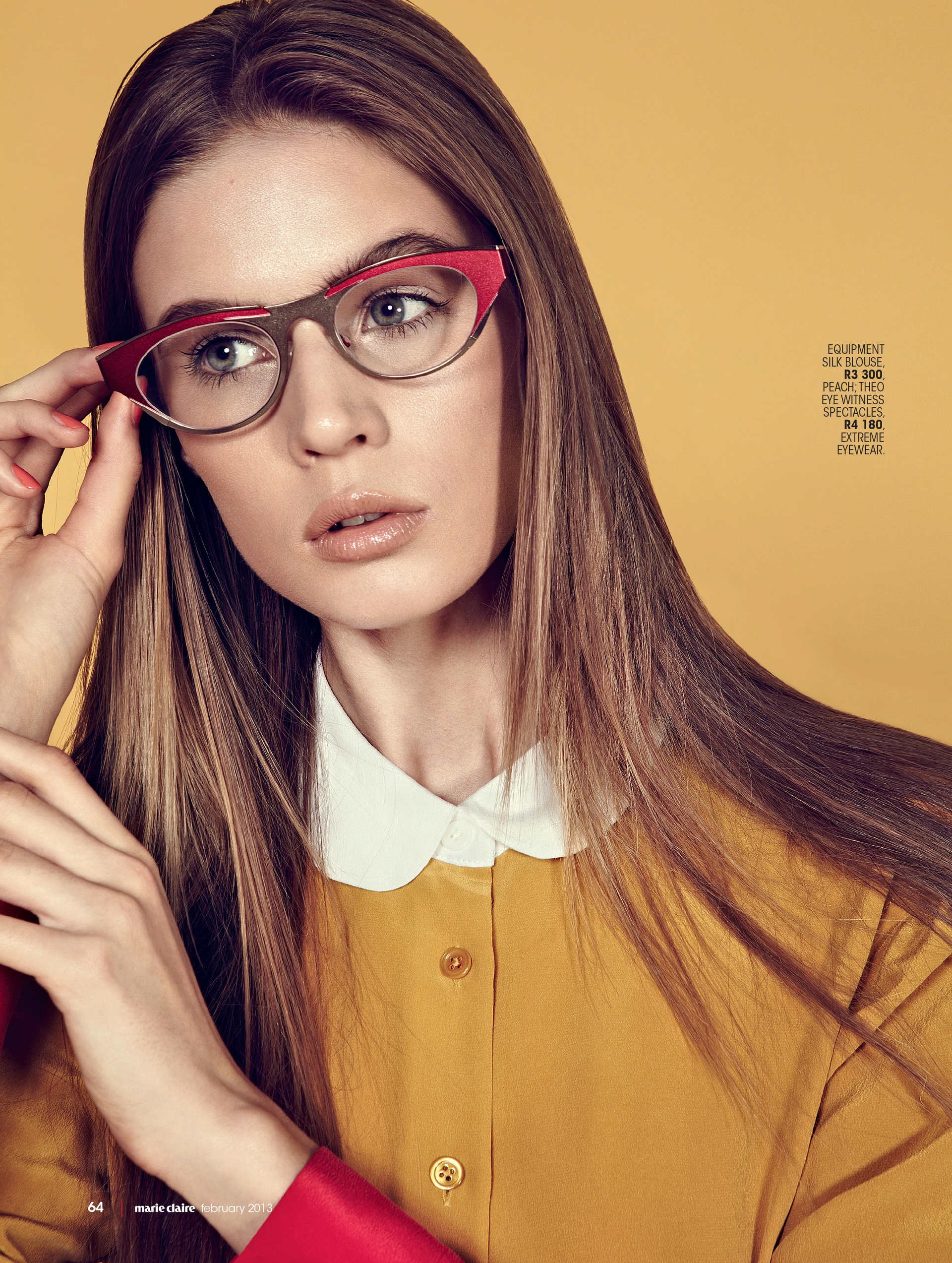 Young woman in a mustard silk blouse with white collar, adjusting red and clear glasses, against a golden background. Fashion shoot for Marie Claire.