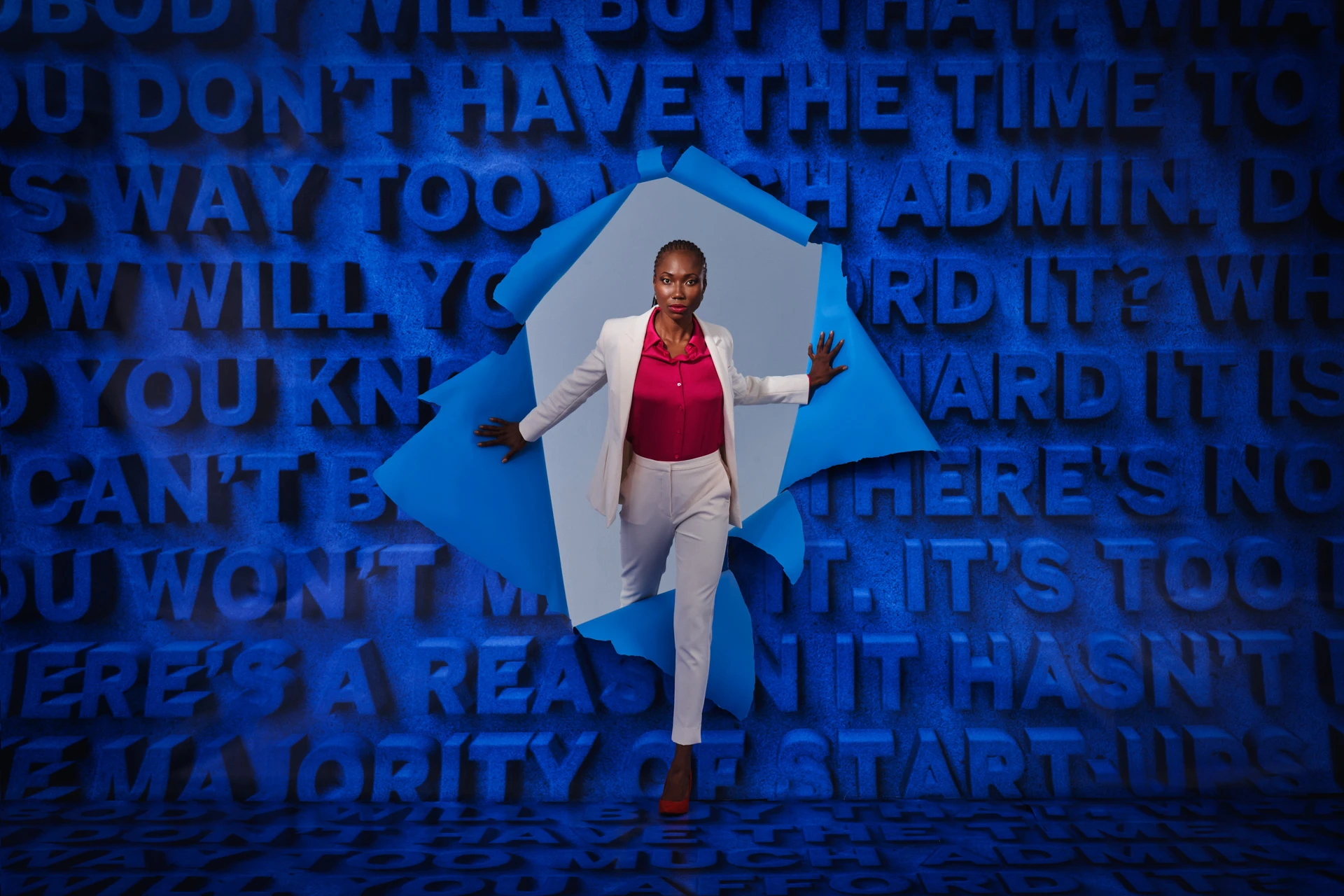 Confident woman breaking through a blue barrier surrounded by motivational text obstacles, symbolizing overcoming startup challenges.