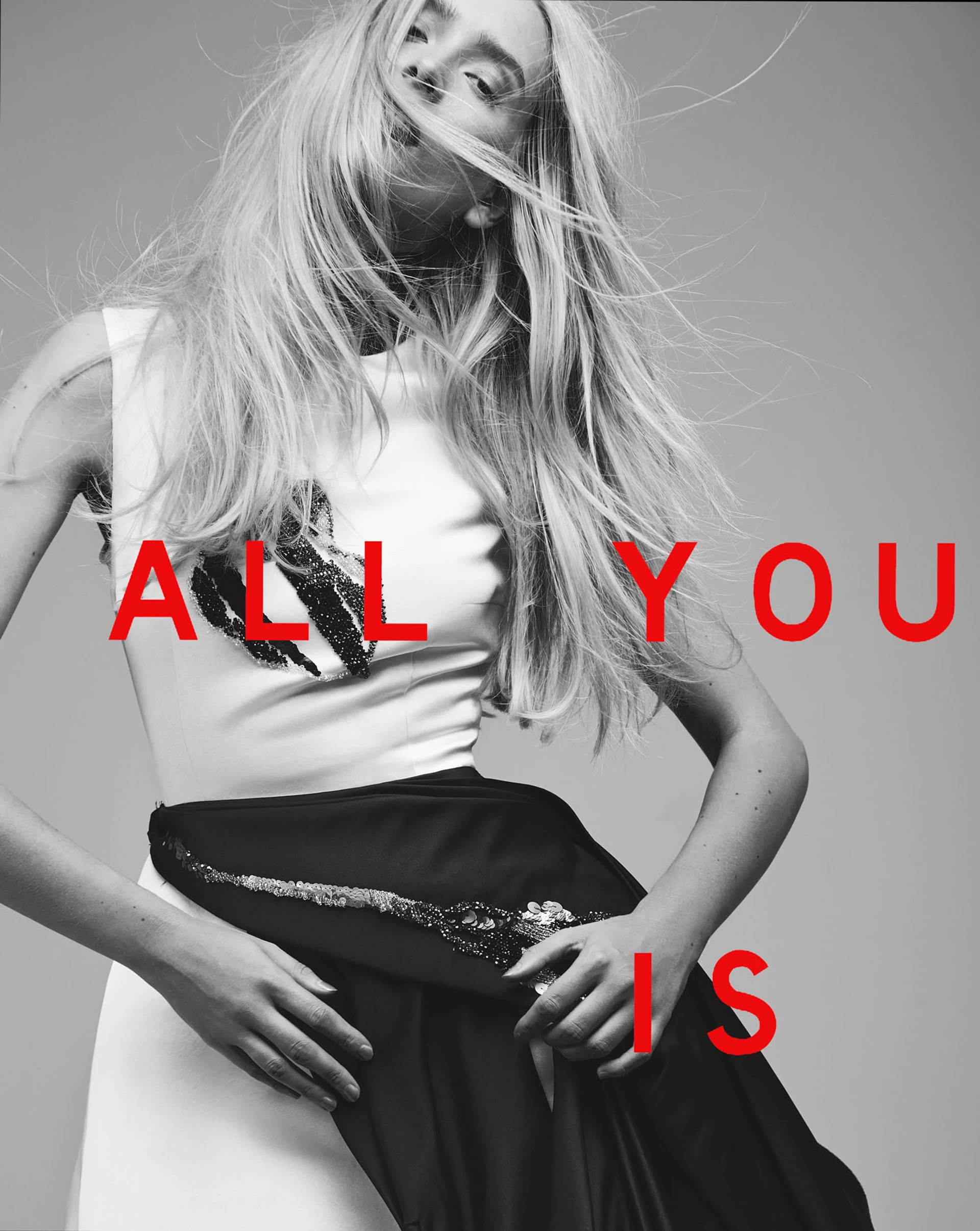 Blonde model with flowing hair wearing a white top with sequin detailing and a black skirt, overlaid with the words 'ALL YOU IS' in bold red letters for Wanted Magazine.
