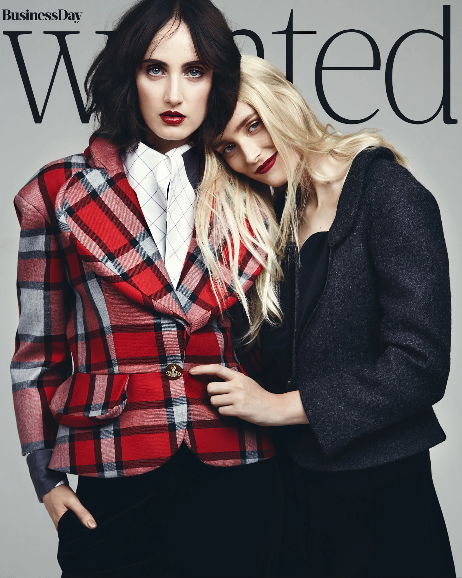 Two models, one with dark hair wearing a red plaid blazer and white shirt, and the other with blonde hair in a black coat, posing intimately for BusinessDay Wanted magazine cover.
